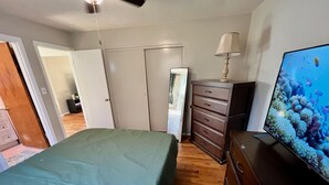 A bedroom with a bed, dresser, TV, and a ceiling fan.