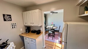 A compact kitchen with white cabinets, a stove, and a refrigerator. There's a dining area with a table and chairs, and a ceiling fan above.