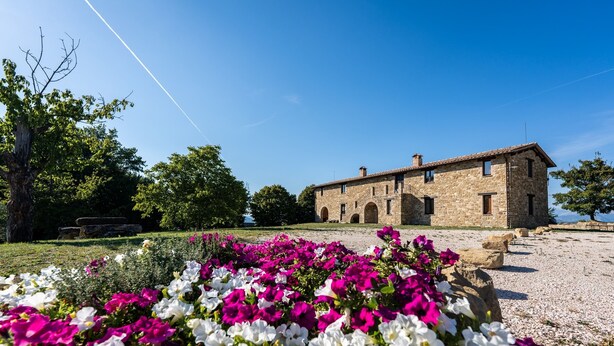 Um edifício de pedra com telhado de telhas, rodeado por uma área de cascalho e flores vibrantes.