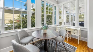 A dining area with a round table, four grey chairs, and a potted plant. Large windows with white frames and a sign reading "SEASIDE" are visible. - Pet Friendly, 150 Yards to Pool, 1 Min to the Beach, Shopping and Dining (Santa Rosa Beach)
