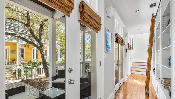 A corridor with a wooden floor, white walls, and a glass door leading to an outdoor patio with wicker furniture and a tree. - Pet Friendly, 150 Yards to Pool, 1 Min to the Beach, Shopping and Dining (Santa Rosa Beach)