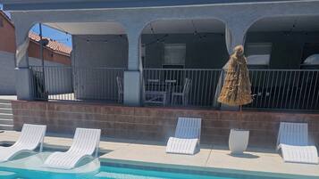 A pool area with white lounge chairs and a covered seating area with a straw umbrella.