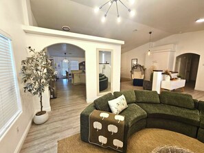 A modern living room with a sectional sofa, a potted plant, and a dining area in the background. - Mountain-View Pool Home w/ Spa & Game Room (Henderson)