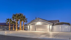 A modern house with a garage and a covered patio area, surrounded by palm trees.