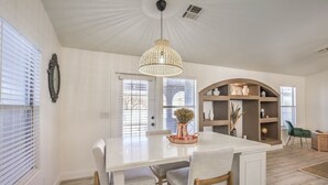 A dining area with a white table, two chairs, a copper vase, and a hanging light fixture.
