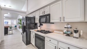 A modern kitchen with white cabinets, a black refrigerator, a microwave, a stove, and a coffee machine.