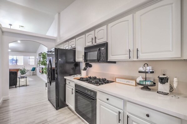 A modern kitchen with white cabinets, a black refrigerator, a microwave, a stove, and a coffee machine. - Desert Chic Vegas Vibes 18 mi to strip, 4 bdrm, Pool + Spa (Henderson)