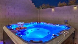 A hot tub with a blue light, surrounded by a brick wall, and a small table with glasses.