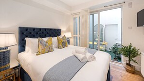 Une chambre d’hôtel avec un grand lit, une table de chevet avec une lampe, une vue sur le balcon extérieur et une plante en pot.
