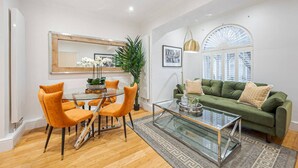 Un salon moderne avec une table basse en verre, des fauteuils orange, un canapé vert et une grande fenêtre donnant sur un beau paysage.