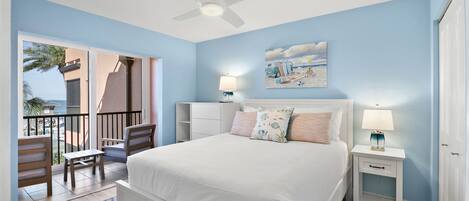A bedroom with a bed, nightstands, a ceiling fan, a painting, and a view of the outdoors.