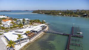 Vista aérea de una propiedad frente al agua con un muelle, un restaurante con terraza y una vista despejada del agua circundante y la costa lejana.