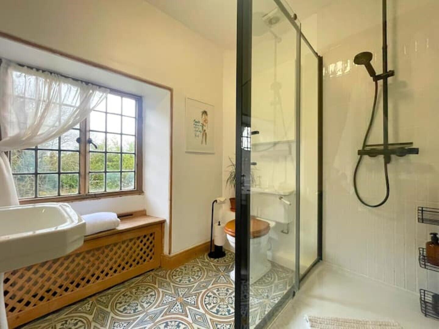 Un baño con ducha envuelta en vidrio, un lavabo y una ventana con vista a zonas verdes.