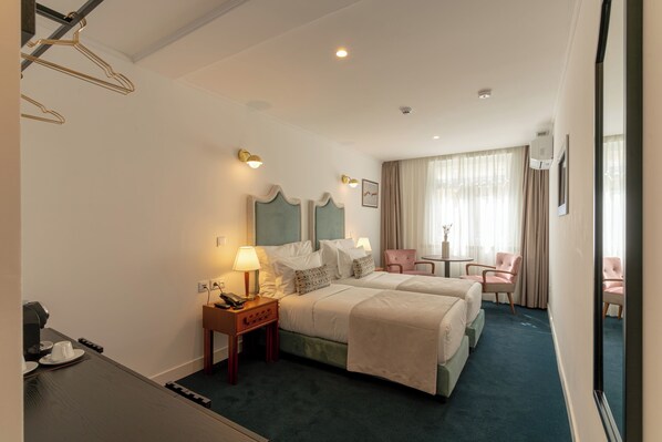 A hotel room with two beds, a desk with a telephone, a chair, and a small table with a lamp.