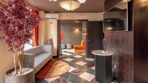 Een moderne lobby met een geruit vloerkleed, een kamerplant, gestreepte banken, een rond tapijt en een ronde tafel met een beeldhouwwerk.