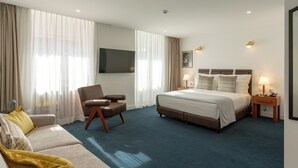 Hotelkamer met een bed, een slaapbank, een stoel, een televisie en een nachtkastje met een lamp.