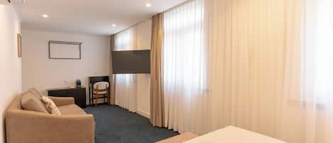 A hotel room with a bed, a sofa, a desk, a chair, and a TV.