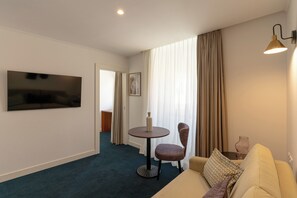 Ett hotellrum med ett runt bord, en stol, en soffa, en tv och ett fönster med gardiner.