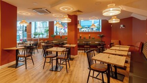 Een restaurant met houten tafels en stoelen, hangende吊灯和 grote ramen met uitzicht op de stad.