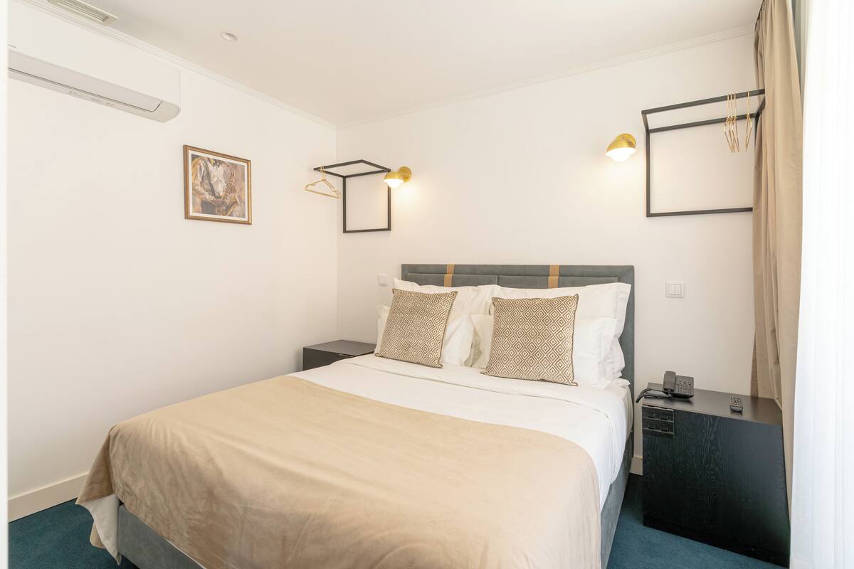 Habitación de hotel ordenada con cama, mesitas de noche, luz empotrada en la pared y un cuadro.
