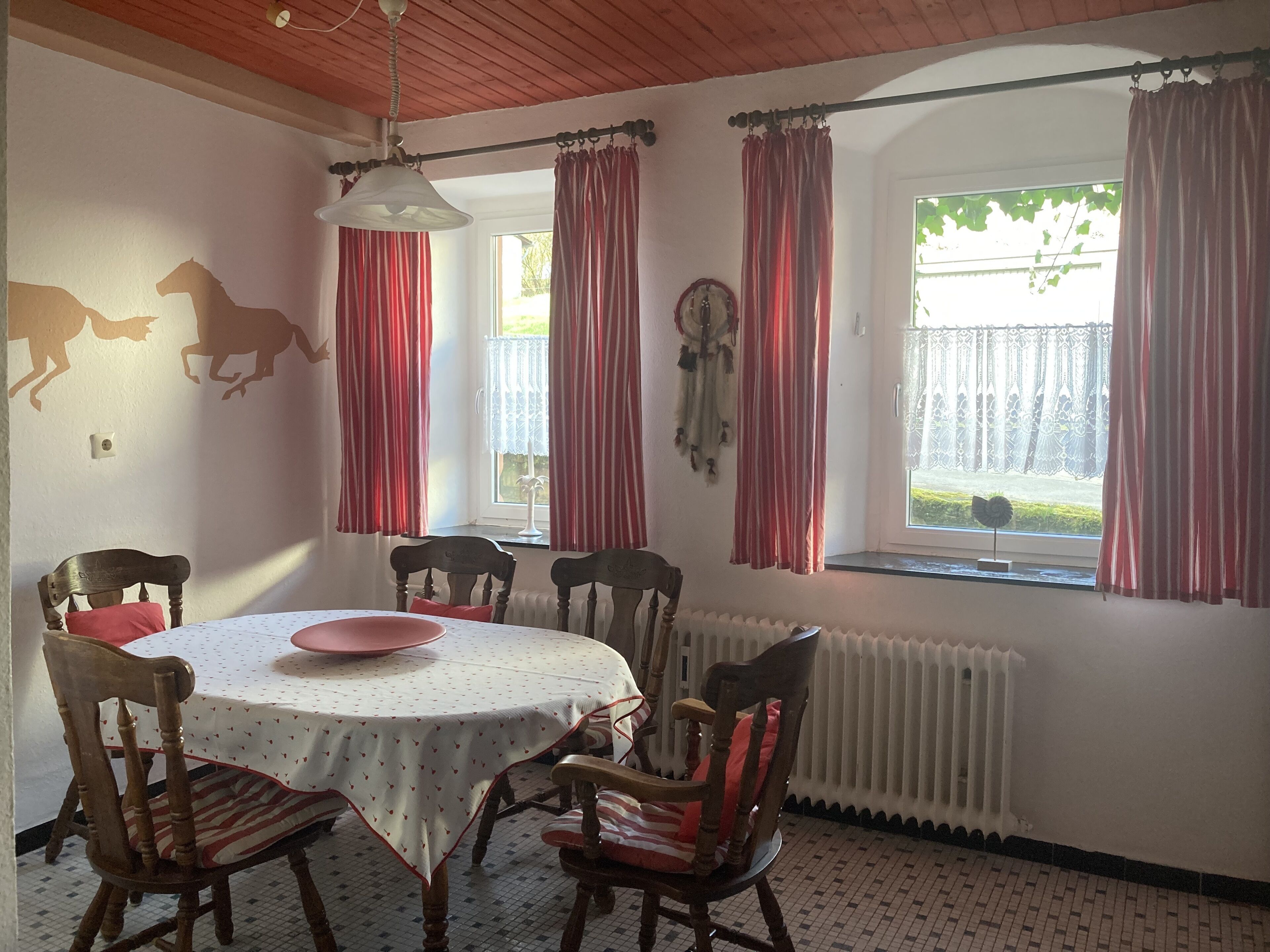 A dining room with a round table, chairs, and a window with curtains.
