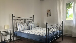 Une chambre à coucher avec un lit en métal, une table de chevet avec une lampe et une fenêtre avec des rideaux.