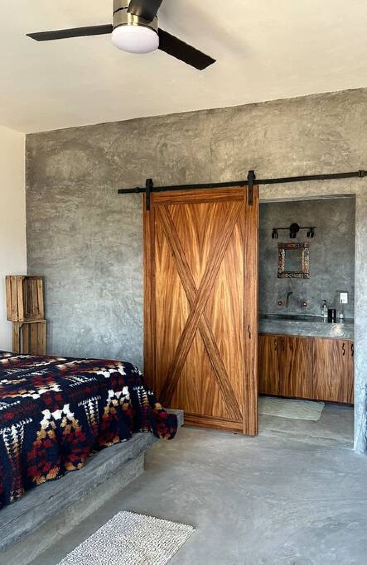 Un dormitorio con cama, ventilador de techo, armario de madera y baño con lavabo y espejo.
