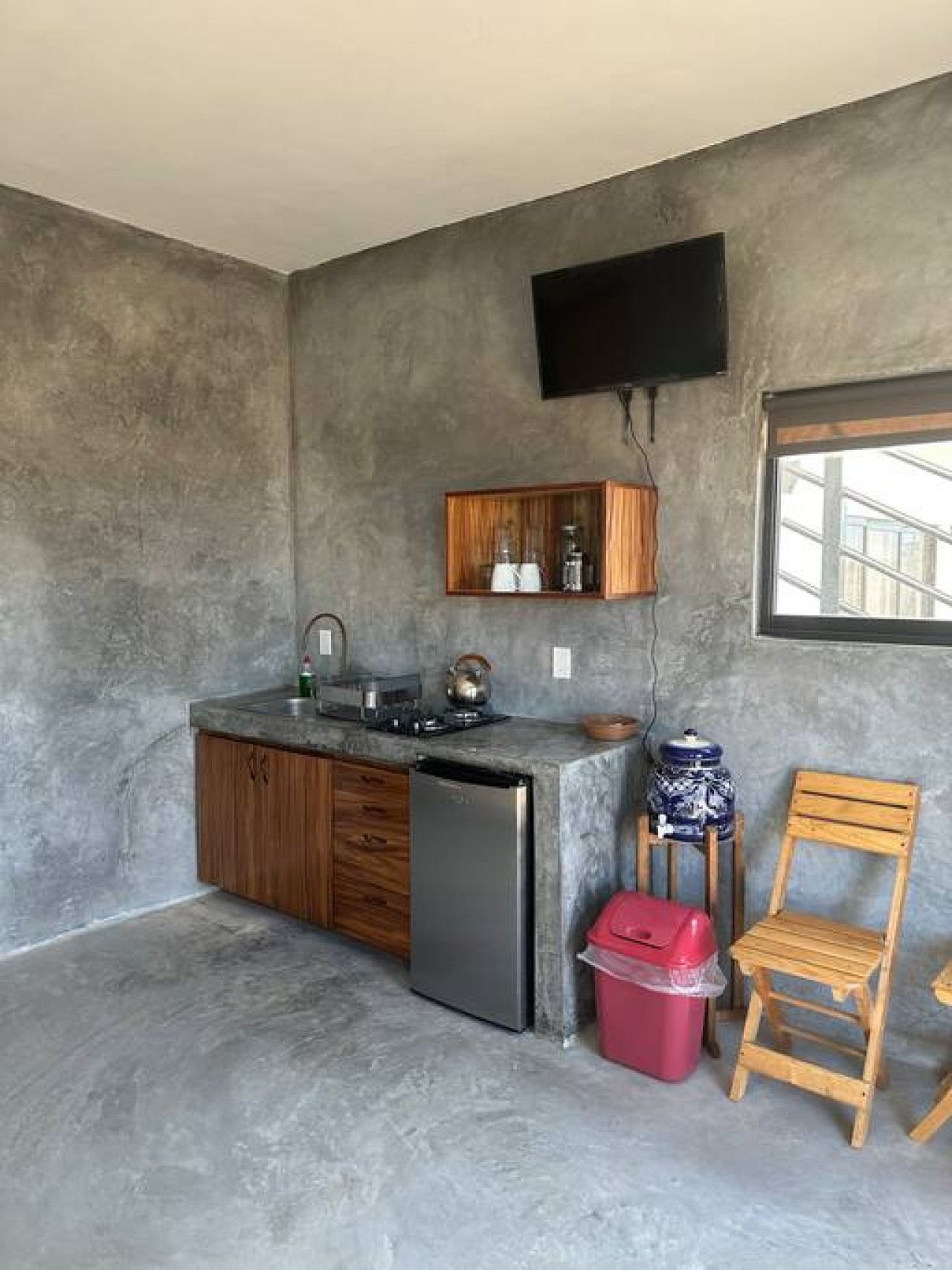 A compact kitchen with a built-in refrigerator, wooden cabinets, a small sink, and a window providing natural light.