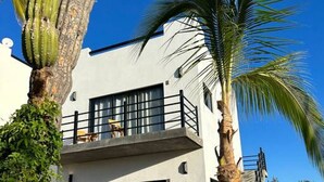 A modern two-story building with a balcony, surrounded by cacti and palm trees. - Condo#5- 5 Min Walk2Beach/Surf-Sleeps4-Queen Suite (Los Cerritos)