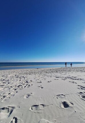 Une plage de sable avec des empreintes et deux personnes qui se promènent.