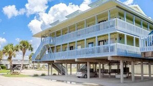 A multi-story hotel with balconies, a covered parking area, and palm trees in the background. - Peaceful Coastal Location Sunsets and Sandy toes! 🩴
6 min walk to the beach ⛱ 
 (Gulf Shores)