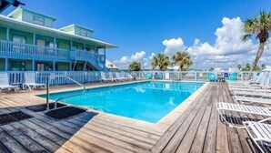 A pool area with a wooden deck, lounge chairs, and a building with balconies. - Peaceful Coastal Location Sunsets and Sandy toes! 🩴
6 min walk to the beach ⛱ 
 (Gulf Shores)