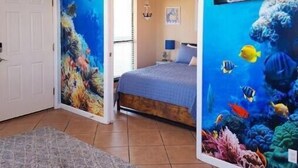 A bedroom with an ocean-themed mural, a bed, a nightstand, and a ceiling fan. - Peaceful Coastal Location Sunsets and Sandy toes! 🩴
6 min walk to the beach ⛱ 
 (Gulf Shores)