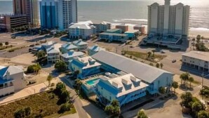 A coastal hotel complex with multiple buildings, including a large structure with a blue roof and several smaller buildings with white roofs. - Peaceful Coastal Location Sunsets and Sandy toes! 🩴
6 min walk to the beach ⛱ 
 (Gulf Shores)