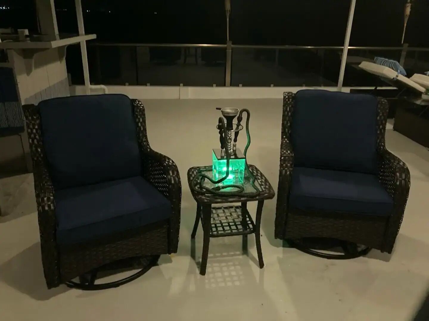 Two wicker armchairs with dark cushions on a balcony with a glass table holding a hookah.