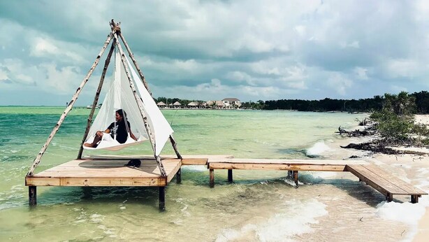 Une jetée en bois s’étendant dans des eaux turquoise et limpides, avec une personne allongée dans un hamac.