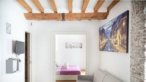 A modern living room with a grey sofa, a painting of a street scene, and a bed with a purple blanket. - Milano Suite Home - Your home in Milan! (Milano)