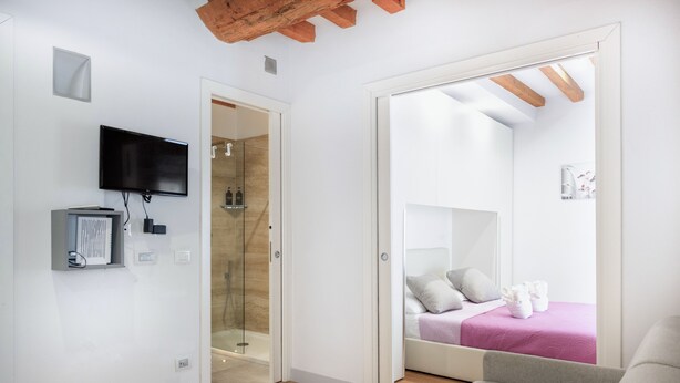 A modern hotel room with a wooden ceiling, a flat-screen TV, a glass shower enclosure, and a bed with a pink bedspread. - Milano Suite Home - Your home in Milan! (Milano)