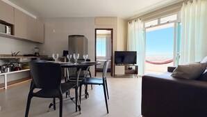 A modern living room with a sofa, a dining area with chairs and a table, a TV, and a view of the beach. - Tranquilidade e muito ventilado  (Aquiraz)