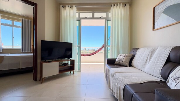 A living room with a television, a sofa, a balcony with a hammock, and a view of the sky. - Tranquilidade e muito ventilado  (Aquiraz)