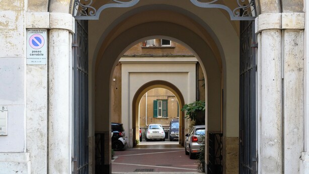 Une entrée en arc surmontée d’un portail en métal, un panneau indiquant qu’il est interdit de se garer, et un chemin pavé menant aux voitures garées.