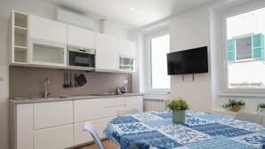 Une cuisine moderne avec des meubles blancs, un four encastré et une grande fenêtre donnant sur un immeuble.