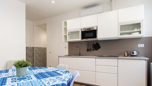 Une cuisine moderne avec des armoires blanches, un four à micro-ondes encastré et un évier. On y trouve une table recouverte d’une nappe bleue et une plante en pot.