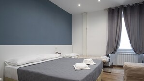 Une chambre avec un grand lit, un plus petit lit, une chaise et une fenêtre avec des rideaux.