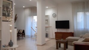 Una sala de estar moderna con un televisor de pantalla plana, un sofá, una mesa de centro y un comedor con sillas y una mesa.