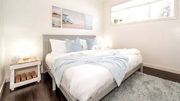 A bedroom with a bed, a nightstand, a window, and wall art.