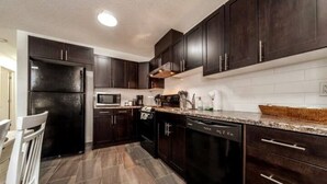 A modern kitchen with dark cabinetry, a stainless steel refrigerator, a microwave, and a dishwasher.