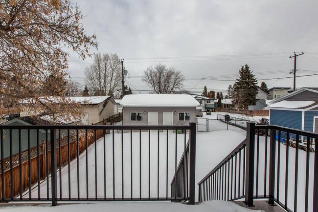 A gated residential area with a snow-covered ground, a metal fence, and houses with snow on their roofs.