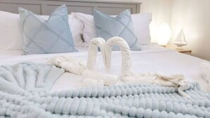 A neatly made bed with a white comforter, blue pillows, and a fluffy blue throw blanket.