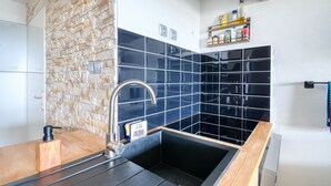 Een keuken met een stenen muur, een zwart betegelde achterwand en een houten aanrecht.